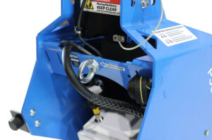 Close-up of a blue industrial machine with a metal winch hook labeled 'WINCH HERE', hoses, and warning labels.